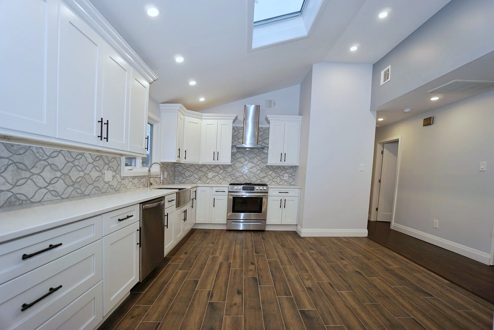 Remodeled kitchen with white cabinets, patterned backsplash, wood-look tile floor